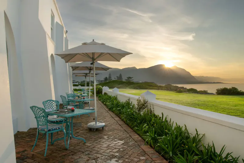 Outdoor patio at The Marine hotel with turquoise chairs, white umbrellas, sunset over mountains and ocean.