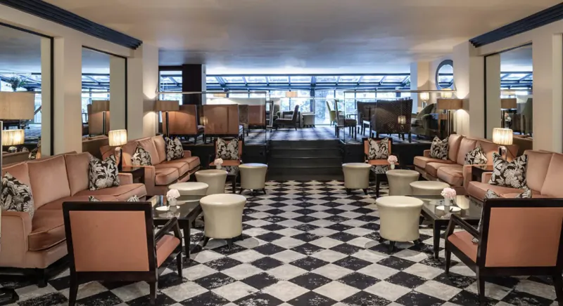 Elegant hotel gallery lounge at The Bristol with pink velvet sofas, black-and-white checkered floor, lamps, and large windows.