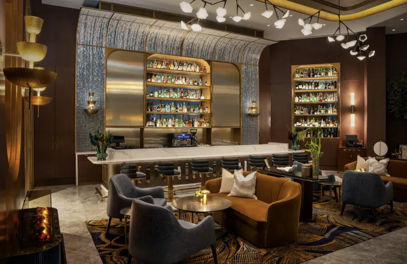 Elegant lounge at Address Grand Creek Harbour with curved gold bar stocked with liquor bottles, pendant lights, plush velvet seating, and plants.