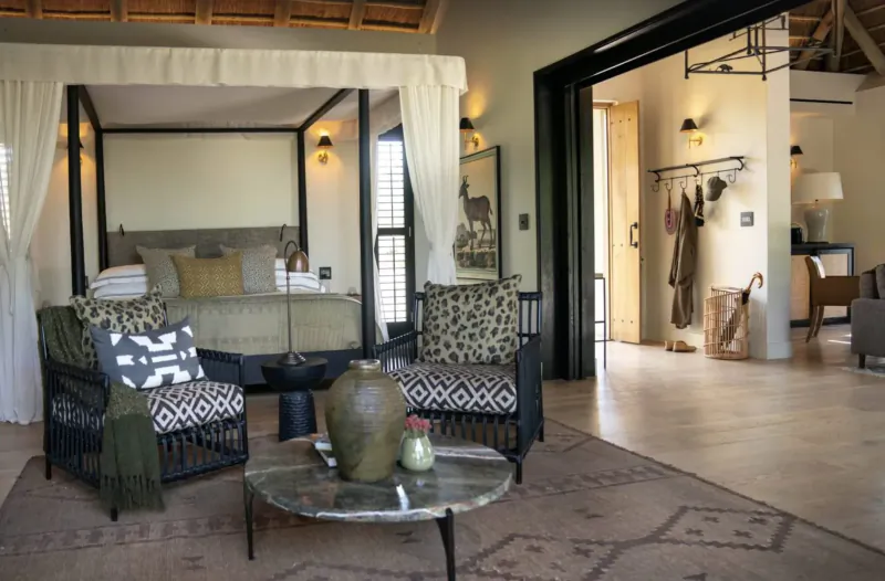 Luxurious bedroom in Monwana Game Lodge with four-poster bed, leopard-print chairs, and safari decor