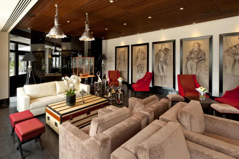 Elegant hotel lounge in Saint-Malo with wooden ceiling, pendant lights, white sofas, red chairs, coffee table, orchids, and large framed portraits.