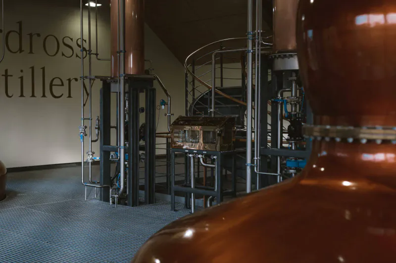 Ardross Distillery interior with large copper stills, pipes, and 'Ardross Distillery' wall text