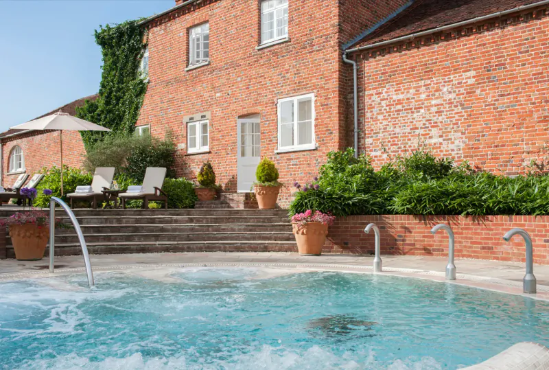 Four Seasons Hampshire: luxurious hot tub by ivy-covered red brick manor house with lounge chairs and gardens