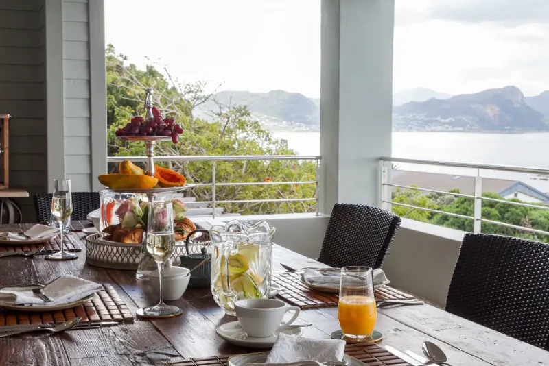 Luxurious outdoor breakfast table with tropical fruits, juices, and ocean-mountain view at coastal retreat.