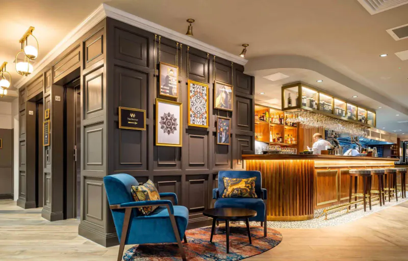 Hotel Indigo Chester lounge: modern wood-paneled bar with orange lighting, blue velvet chairs, art on walls.