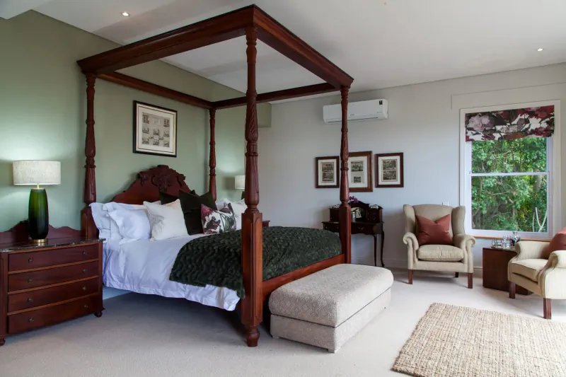 Elegant bedroom at Tintswalo Boulders Boutique Hotel with four-poster bed, green bedding, armchair, and garden window view.