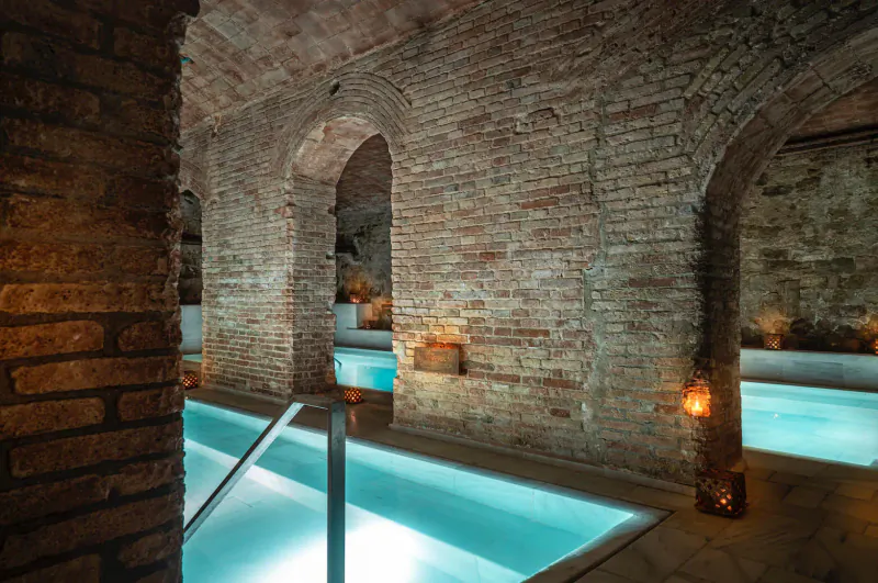 Candlelit indoor pool in brick arched vault at Aire Ancient Baths, glowing turquoise water and steps.