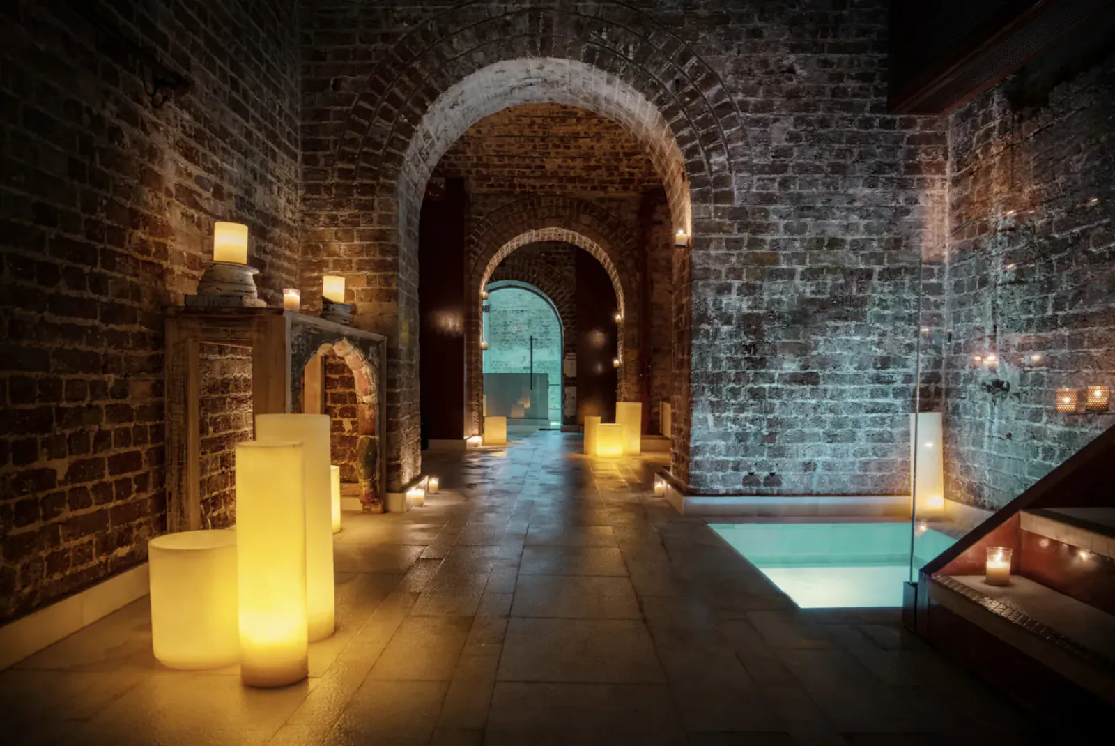 Candlelit brick arched corridor in Aire Spa at St. Martins Lane Hotel, leading to glowing pool.