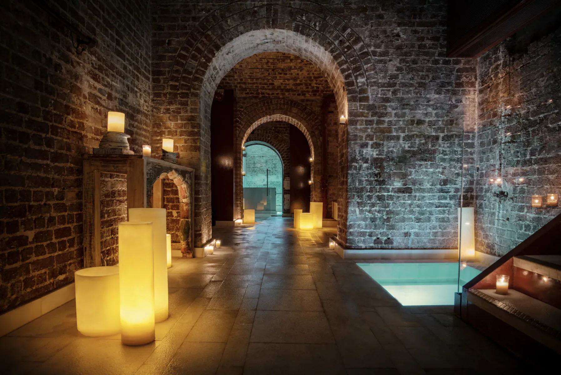 Candlelit brick arched corridor in Aire Spa at St. Martins Lane Hotel, leading to glowing pool.