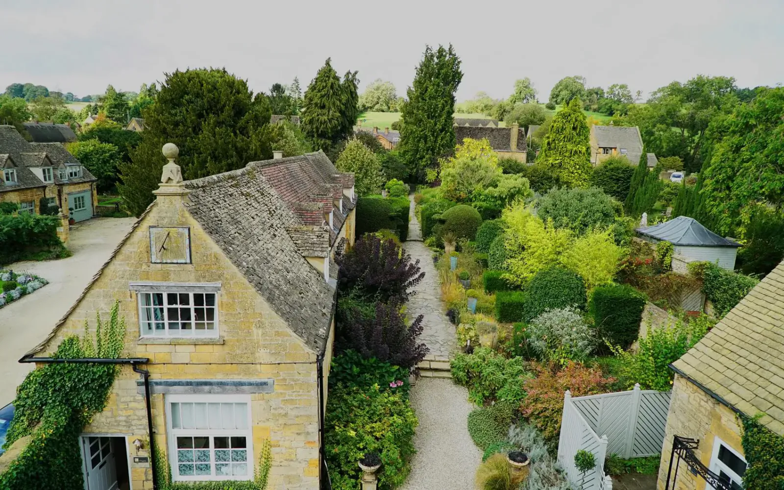 Aerial view of Cotswold House Hotel & Spa, a stone manor with lush gardens, trees, and surrounding countryside cottages.