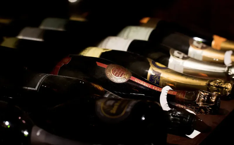 Rows of Vivat Bacchus champagne bottles in a dimly lit rack, some with red labels and foil tops.