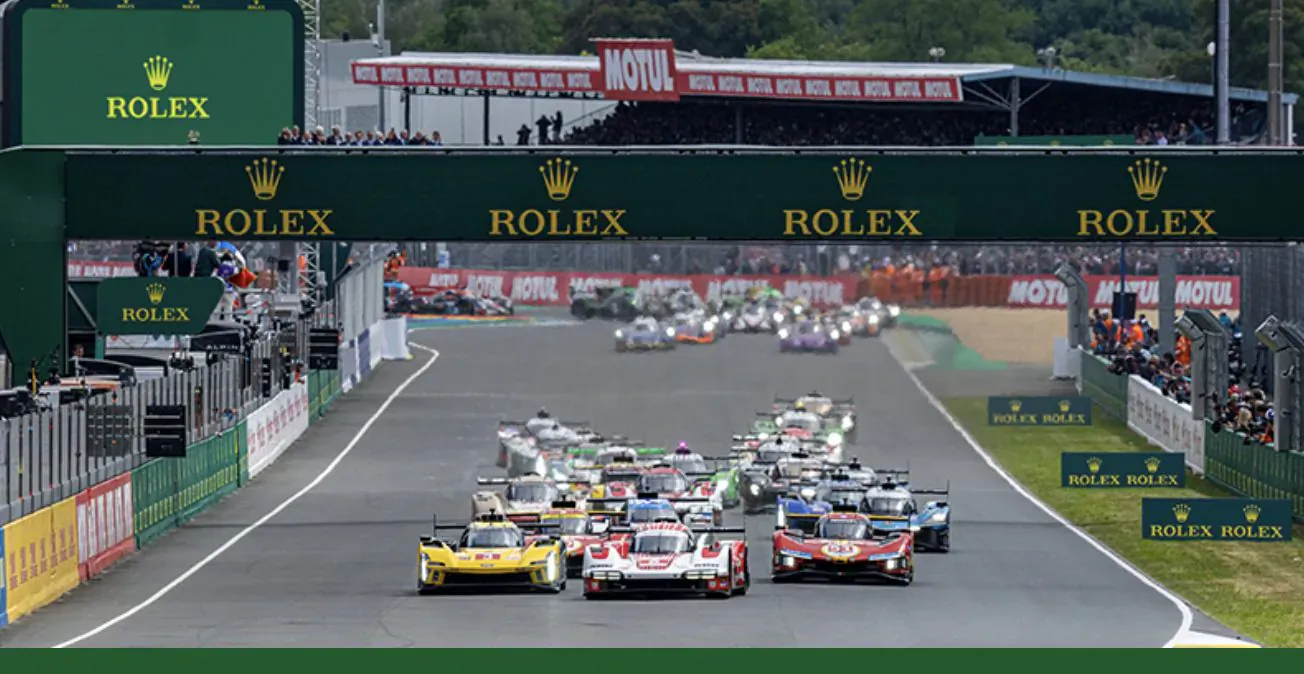 24 Hours of Le Mans race: pack of colorful prototype cars speeding under Rolex-branded green grandstand