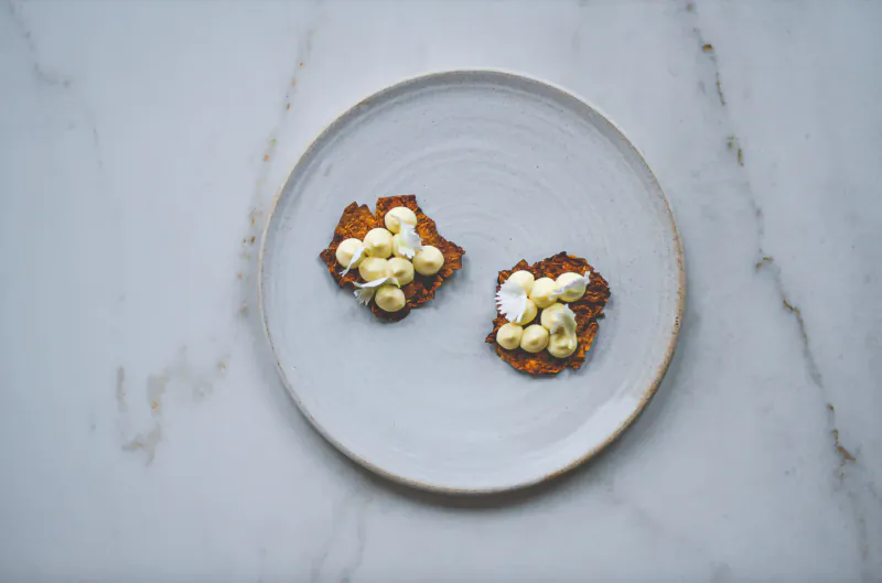Two orange latkes topped with white dollops on a white plate on marble surface