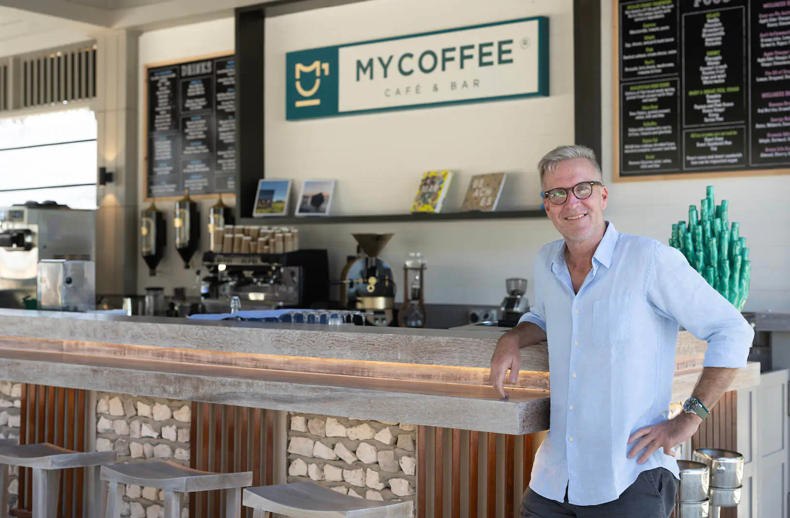Martin, MD of Cora Cora, smiling at MyCoffee Cafe Bar counter with espresso machines and menu boards
