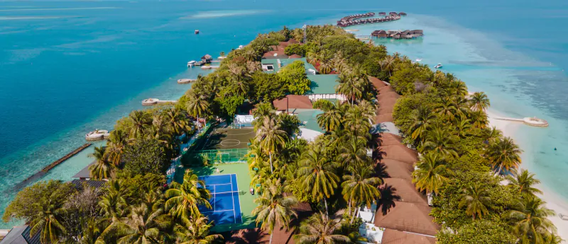 Aerial view of Lily Beach Resort & Spa, Maldives: overwater villas, tennis court, palm-fringed paths, turquoise lagoon.