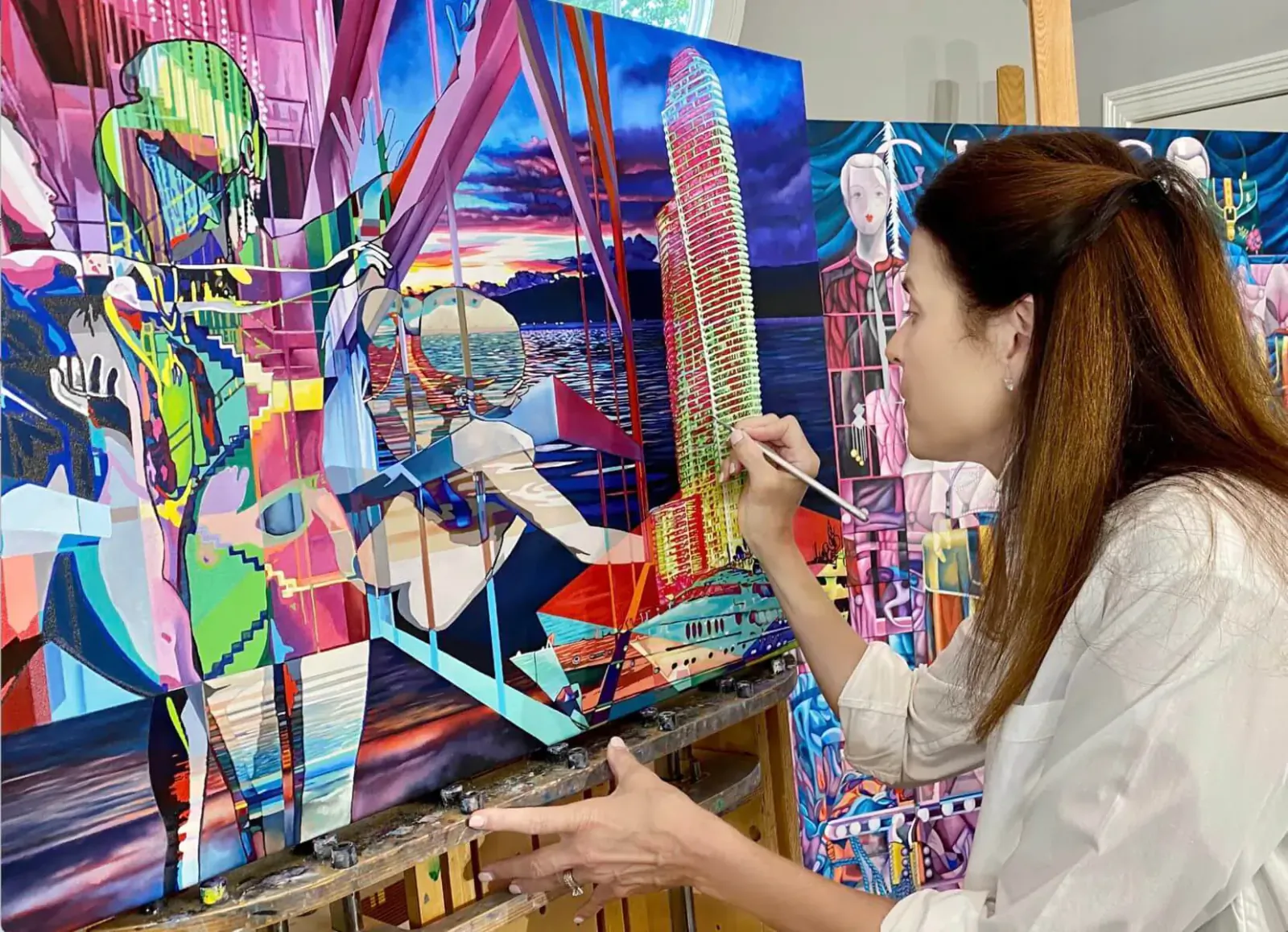 Woman with brown hair painting vibrant abstract artwork of figures and sunset in art gallery studio