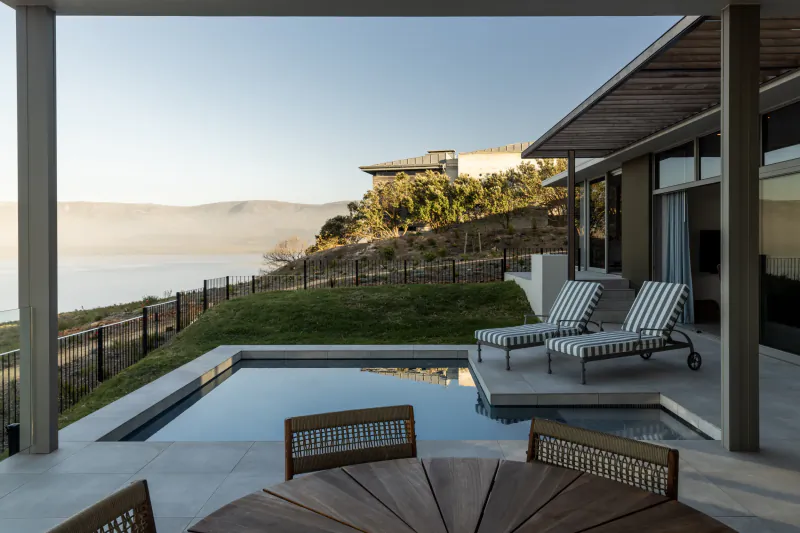 Infinity pool and striped lounge chairs on terrace overlooking ocean and mountains at Benguela Cove wine estate