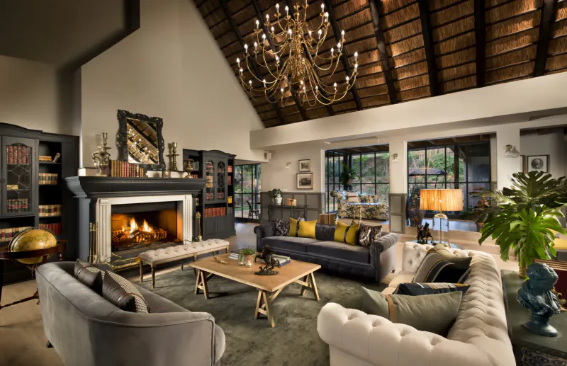 Elegant lounge at Stanley & Livingstone Boutique Hotel with chandelier, fireplace, plush sofas, bookshelves, and large windows.