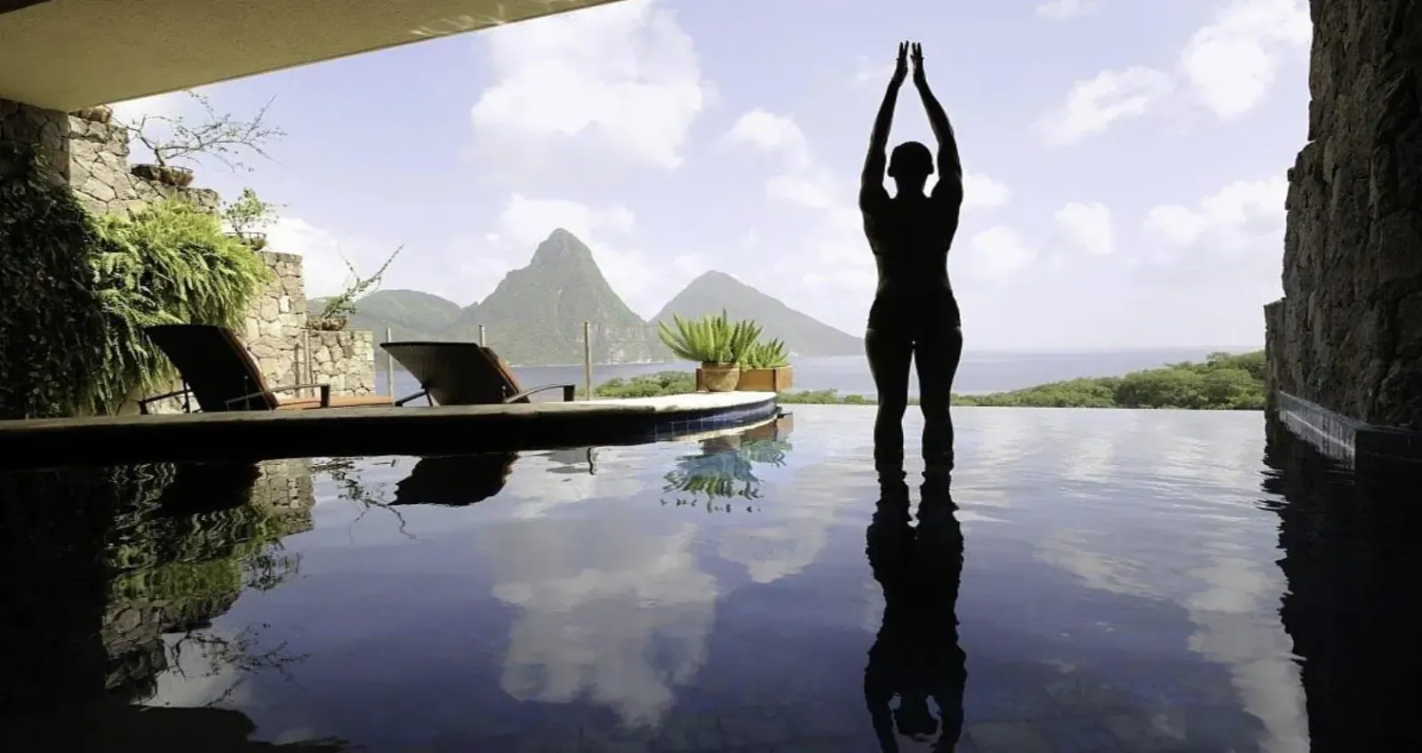 Silhouette of woman in yoga pose at infinity pool edge, Pitons mountains and ocean view, wellness retreat.