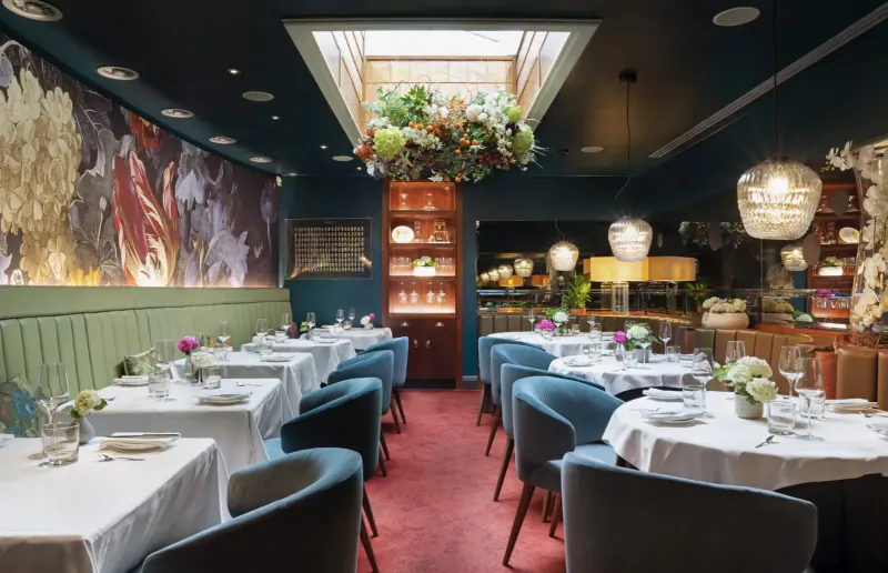 Elegant dining room at Pied à Terre with floral wall murals, skylight, velvet chairs, set tables for cooking masterclass.