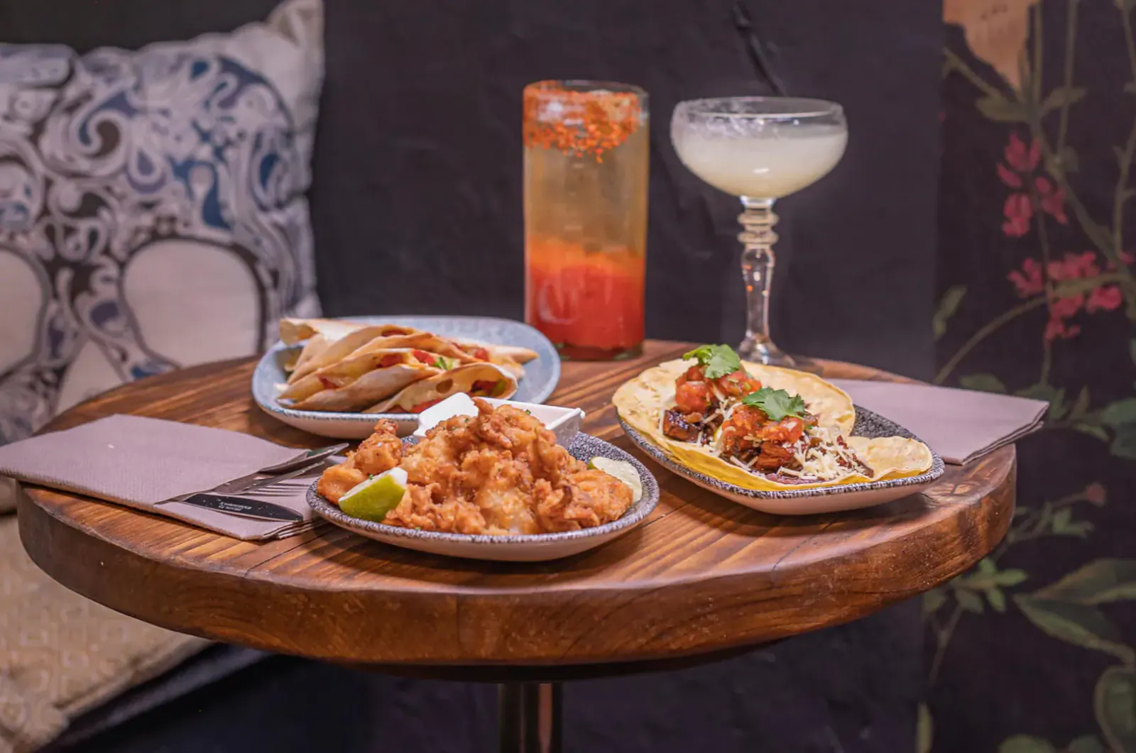 Wooden table with shrimp tacos, fried shrimp, and margarita at Mezcalito Mexican bar.