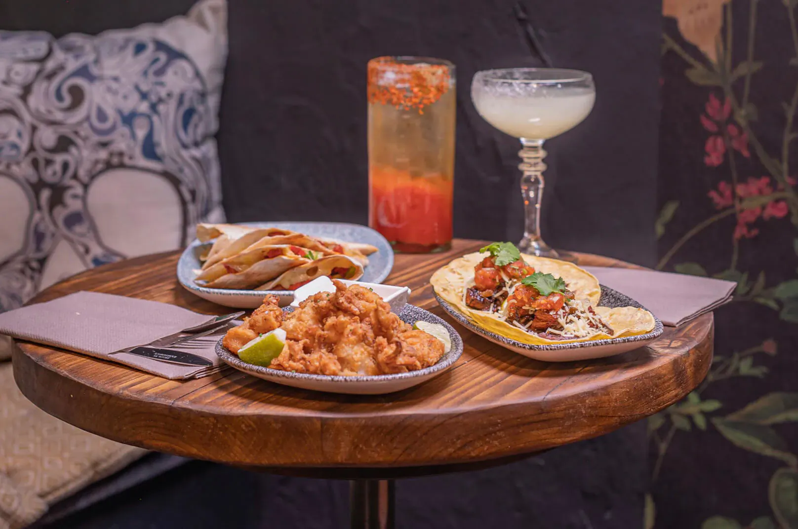 Wooden table with shrimp tacos, fried shrimp, and margarita at Mezcalito Mexican bar.