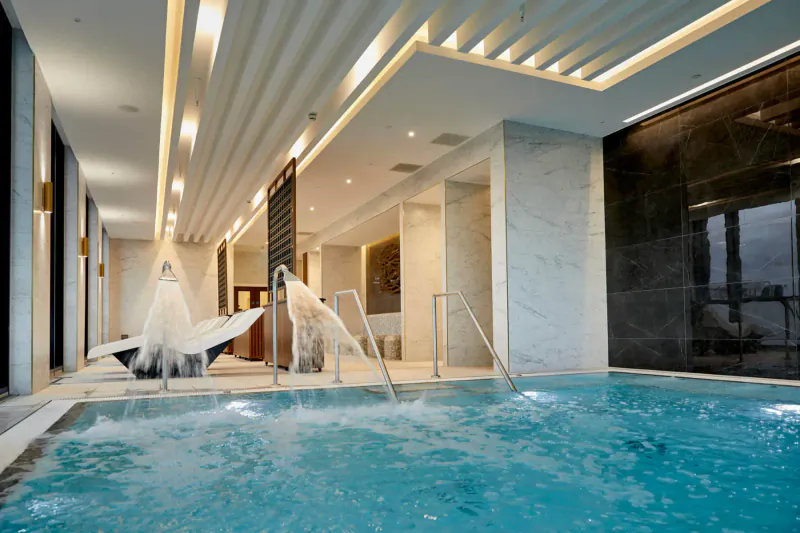 Luxurious indoor infinity pool with cascading water, white umbrellas, marble walls, and modern lighting in city centre setting.