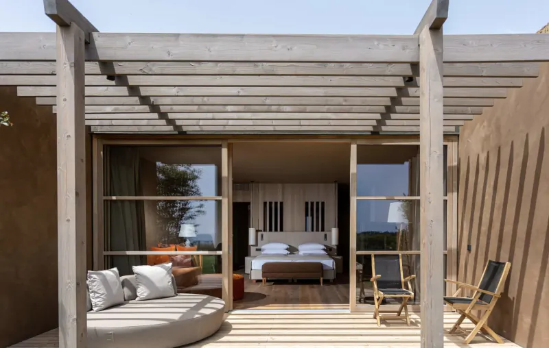 Open wooden pergola terrace of ADLER Spa Resort Sicily with curved sofa, chairs, and bed visible through glass doors