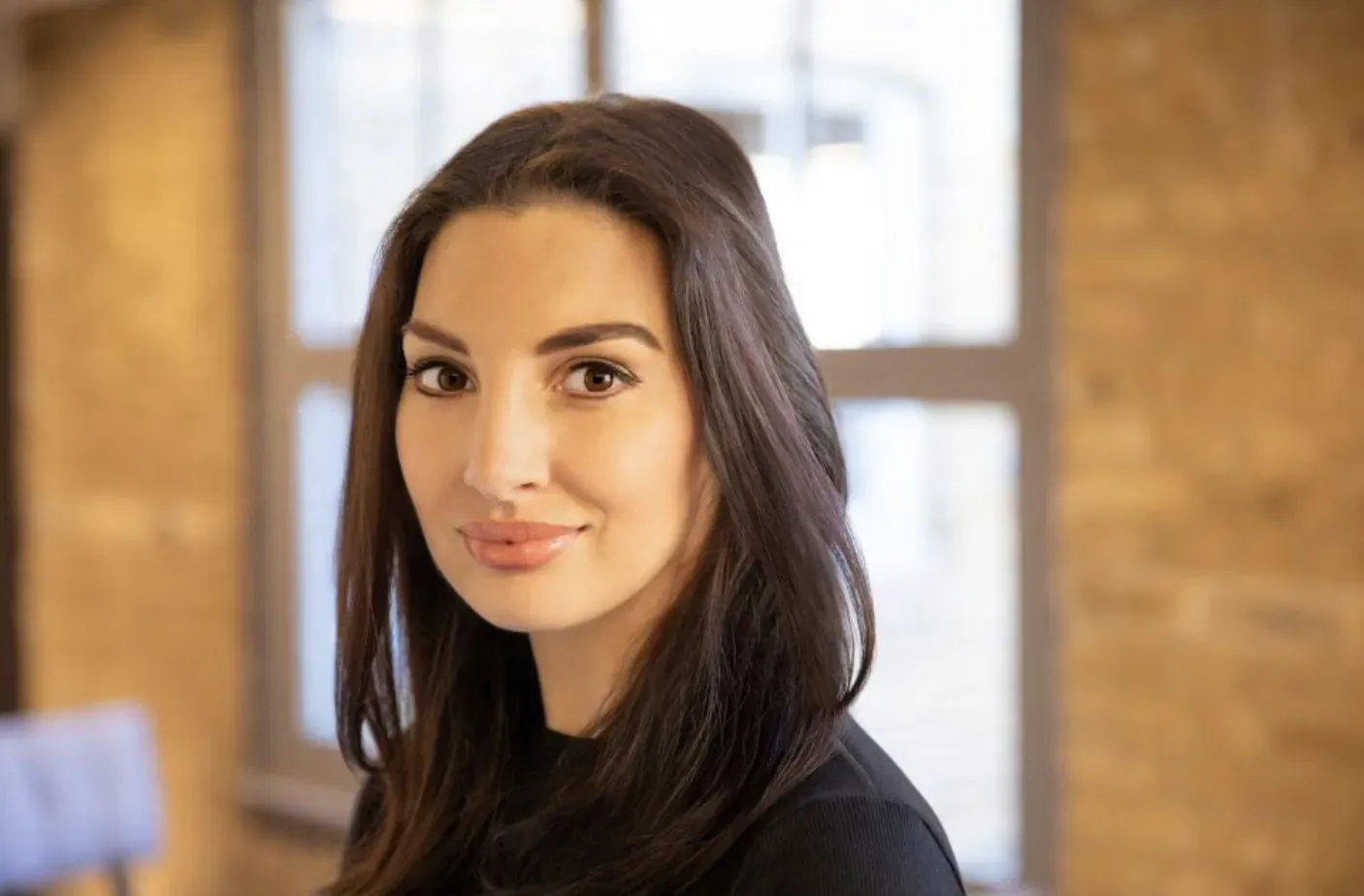 Dr Jana Vogt smiles in black top against brick wall window in office interview setting