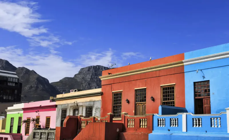 Colorful Bo-Kaap houses in vibrant pinks, blues, reds, and greens against Table Mountain under blue sky.