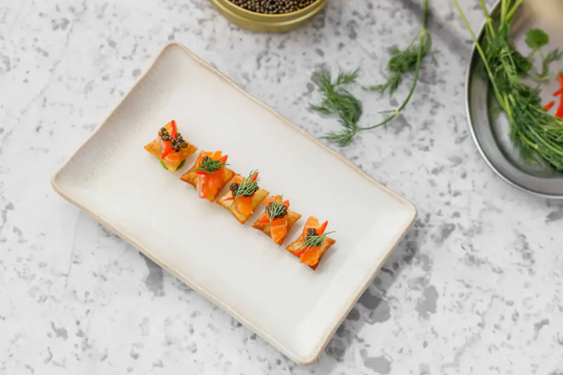 Six orange carrot slices topped with green herbs on a white rectangular plate, garnished with dill sprigs on a quartz surface.