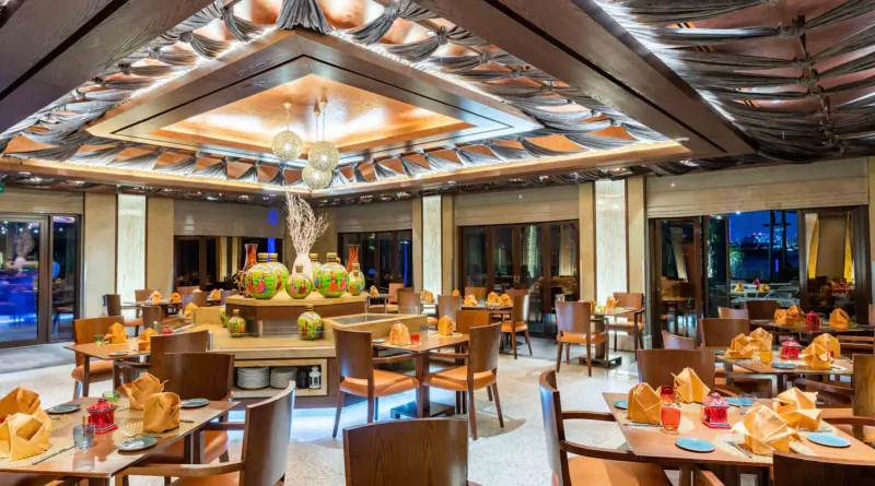 Elegant Sofitel Dubai restaurant with ornate ceiling, balloons, coconut centerpieces, and wooden tables set for dining.