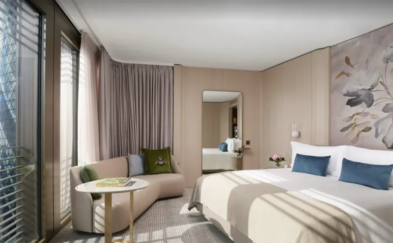 Luxurious Pan Pacific London hotel suite with curved sofa, king bed, floral wall art, and city view.