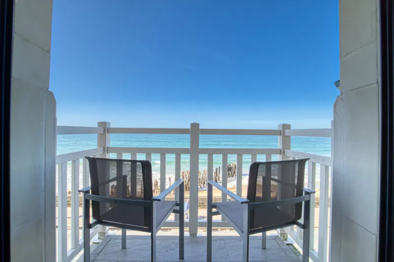 Two lounge chairs on a white balcony overlooking the beach and blue sea at Hotel Nouveau Monde Saint-Malo.