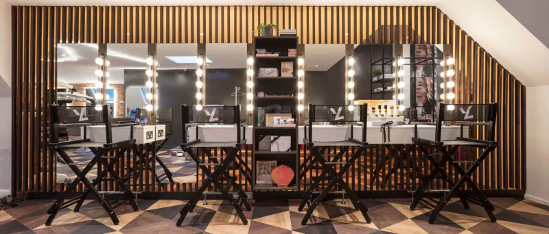 Modern makeup vanity stations with black stools, LED mirrors, and wood-paneled walls in a medispa gallery