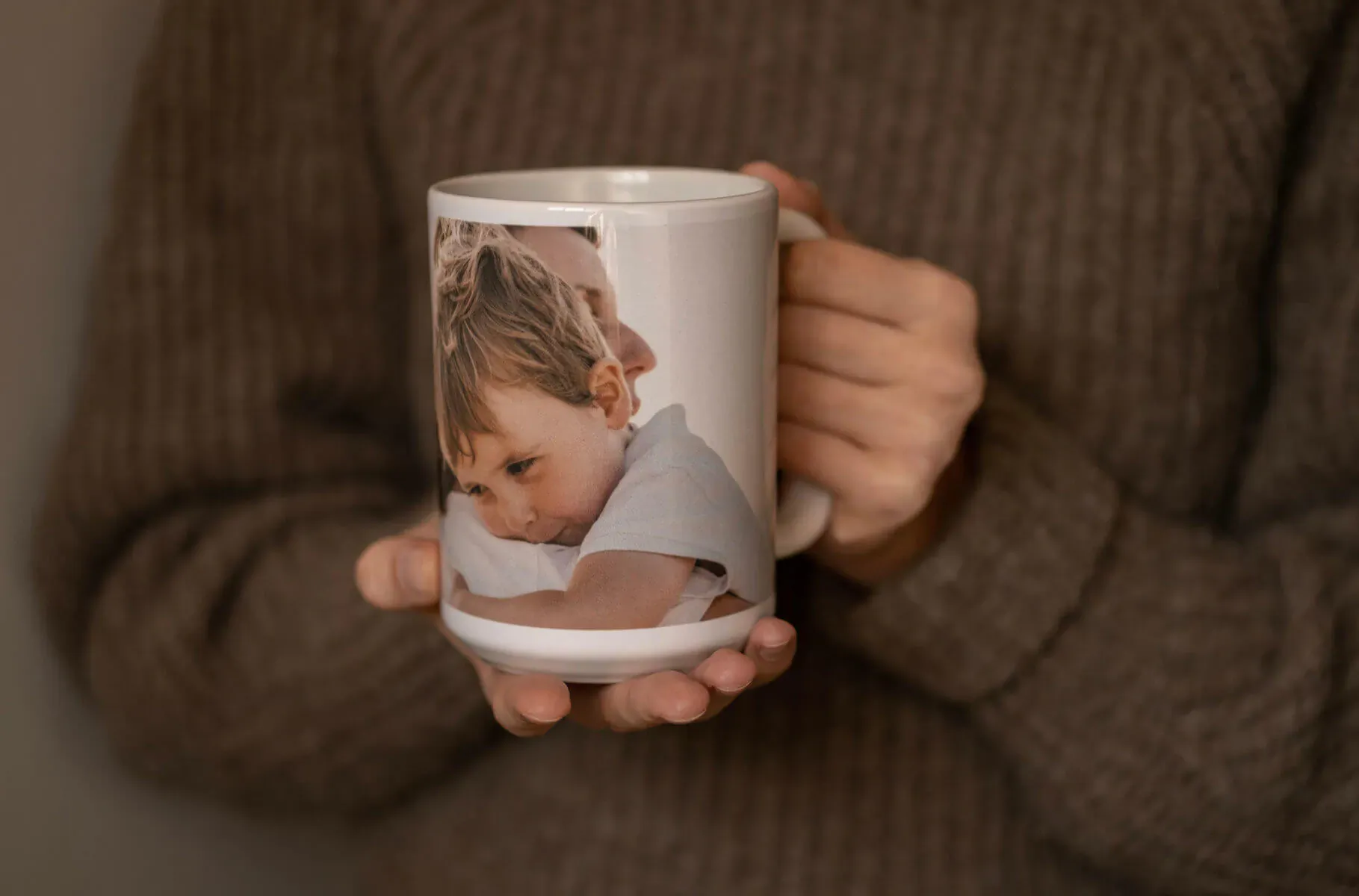 Hands holding white mug with photo of curly-haired baby boy in blue shirt, Father's Day gift idea