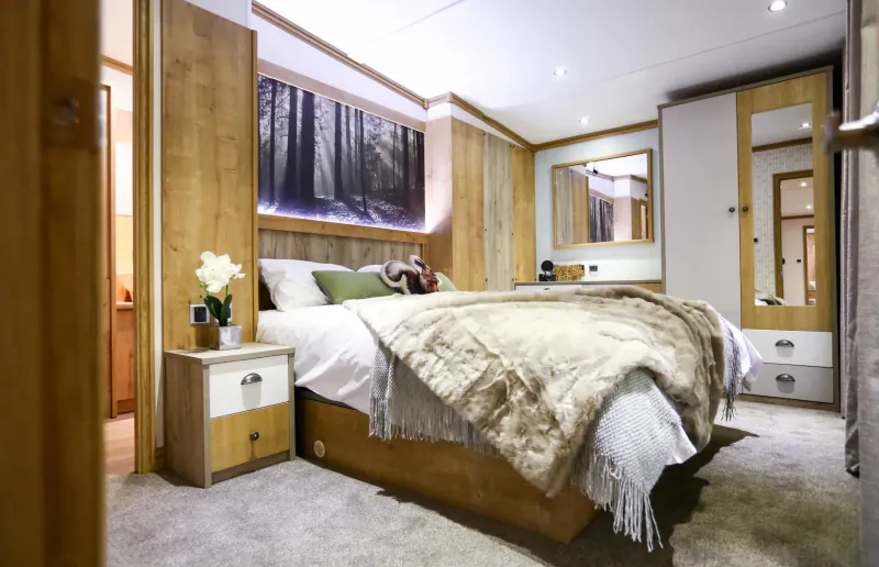 Luxurious wooden bedroom in New Forest cabin with forest wall art, white duvet, fur throw, orchids, and mirrored wardrobe.