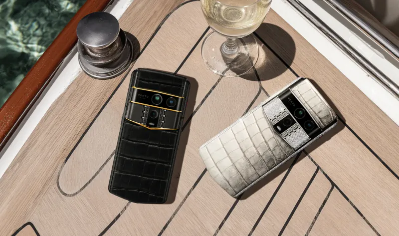 Black and white crocodile-textured Vertu phones beside wine glass on luxury yacht deck.