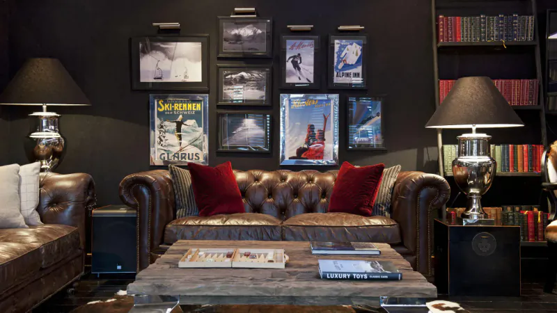 Cozy lodge lounge with leather sofa, coffee table, ski posters on black wall, bookshelves, and lamps