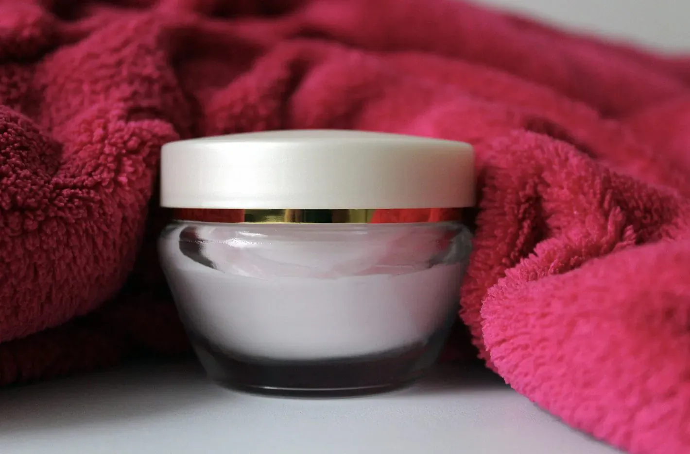Open white jar of white skincare cream on pink towel, skincare routine featured
