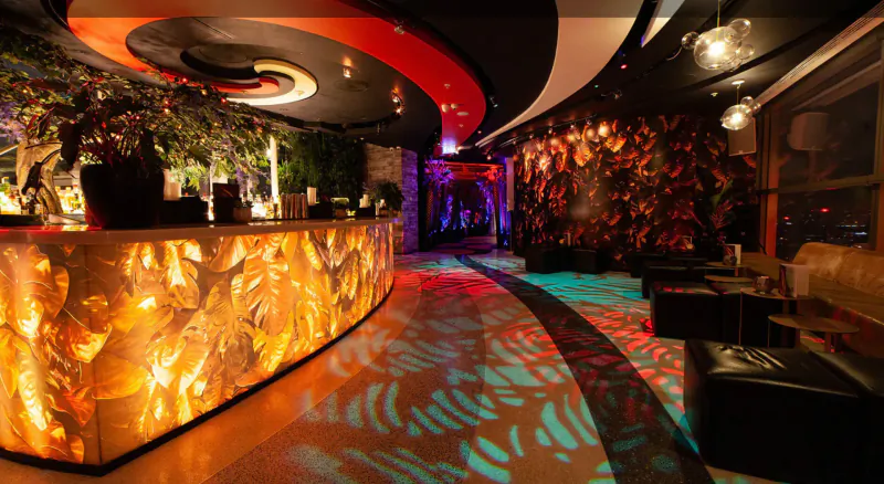SushiSamba gallery: Curved glowing orange bar with plants, neon-lit lounge, patterned floor, city view