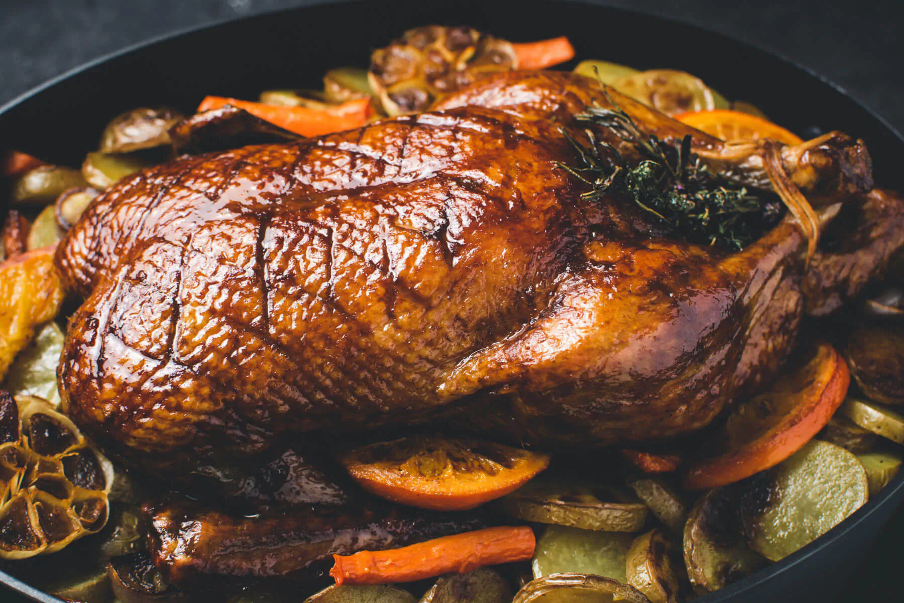 Roast duck in black pan with carrots, onions, garlic, orange slices, and herbs