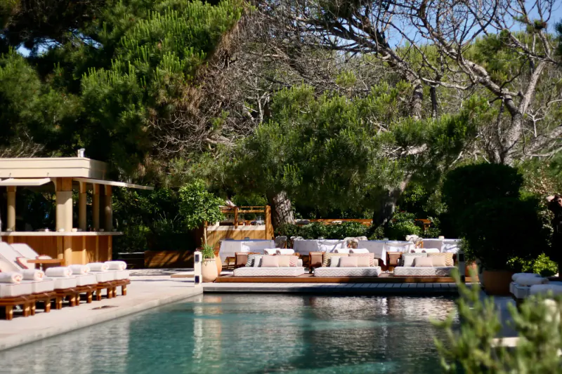 Luxurious Gigi Rigolatto beach house poolside with beige loungers, wooden bar, and pine trees in Dubai