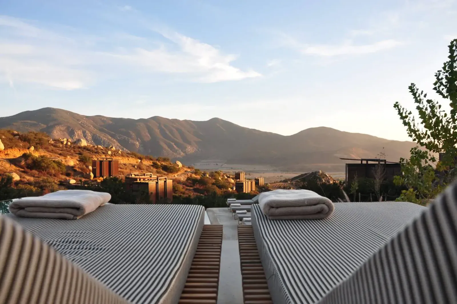 Close-up of two striped lounge chairs with white towels at luxury pool overlooking sunset mountains.