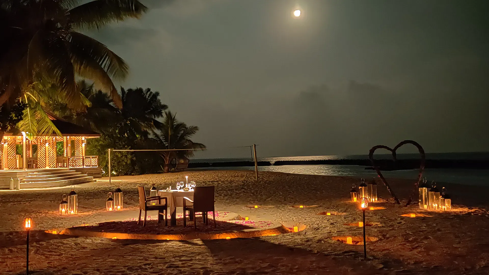 Romantic candlelit beach dinner for two at Valentine's Lily Beach Resort under full moon and palm trees