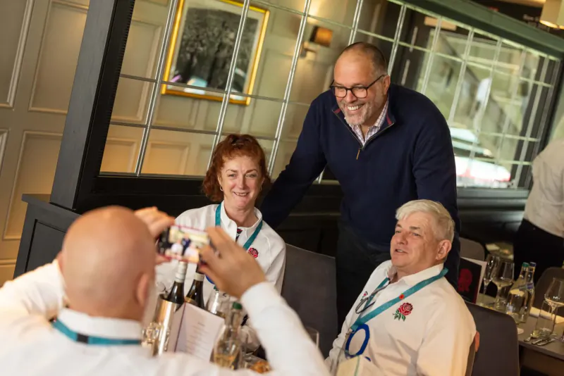 Three people in Team GB lanyards and England Rugby badges smiling at a candlelit hospitality dinner table