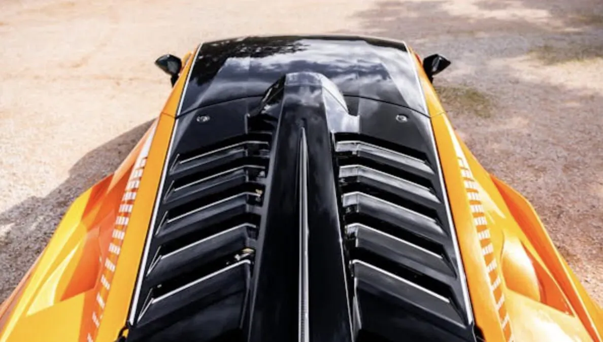 Close-up rear view of sleek orange luxury sports car with black aerodynamic vents on sandy ground