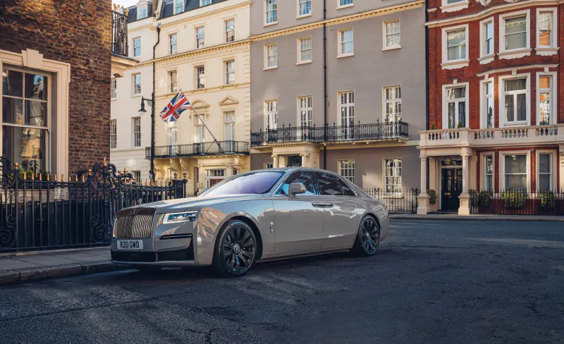 Silver Rolls-Royce Ghost parked on London street with Union Jack flag and Georgian townhouses.