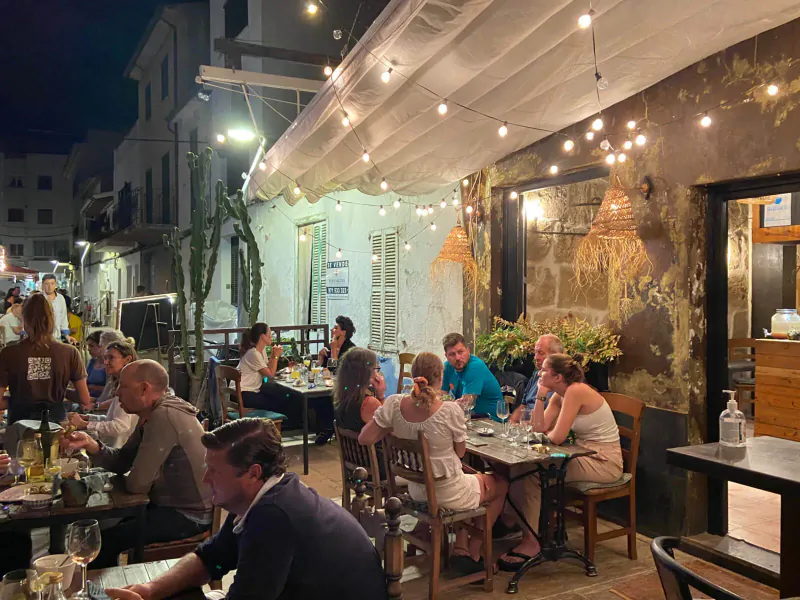 Outdoor evening dining at Terrae Restaurant in Pollenca: diverse group at tables under string lights and canopy.