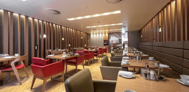 Elegant Apex Temple Court hotel dining room with red chairs, wooden tables set with plates, warm lighting.